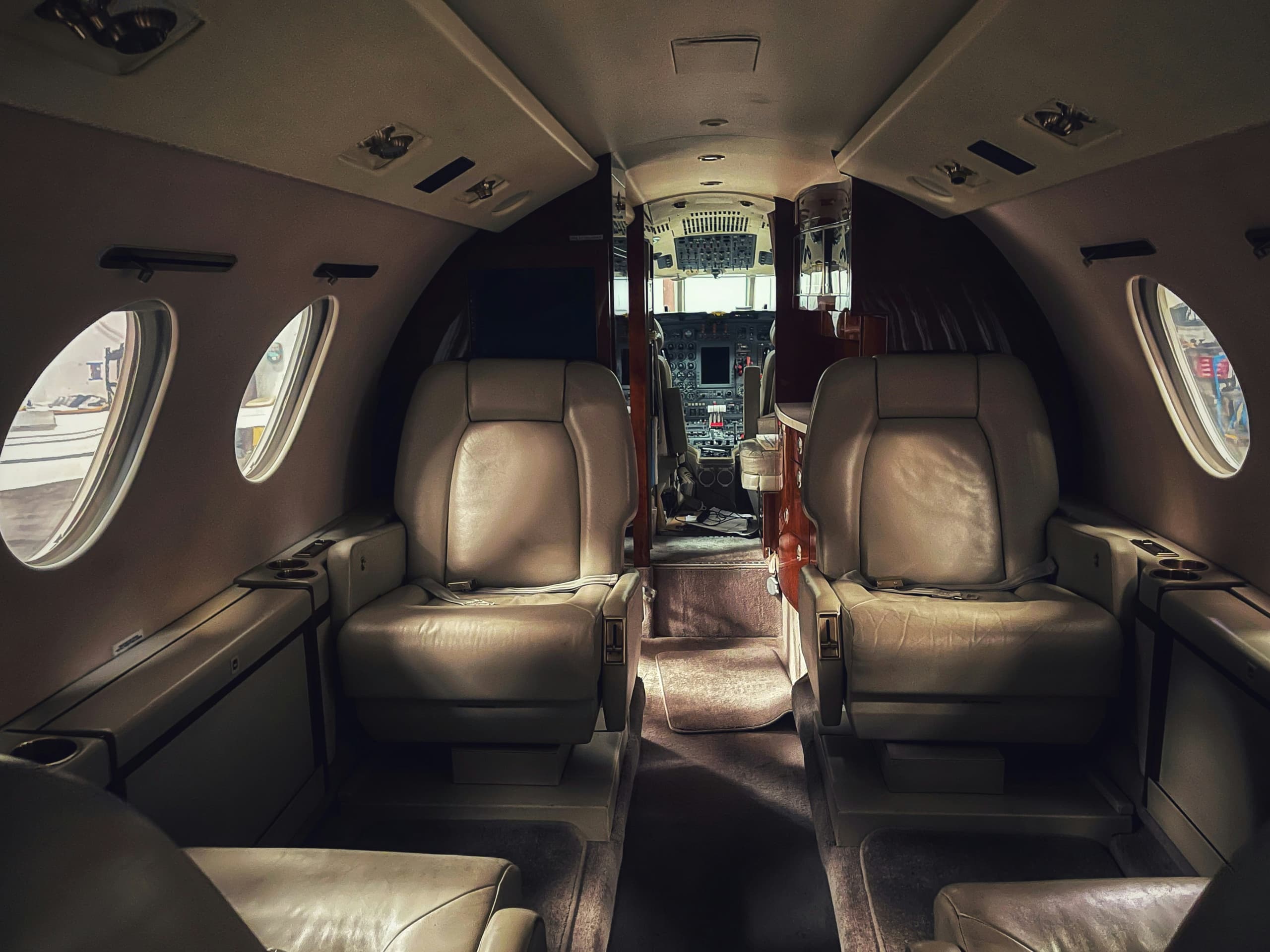 Cream leather club seats facing each other in a private jet cabin, cockpit visible beyond